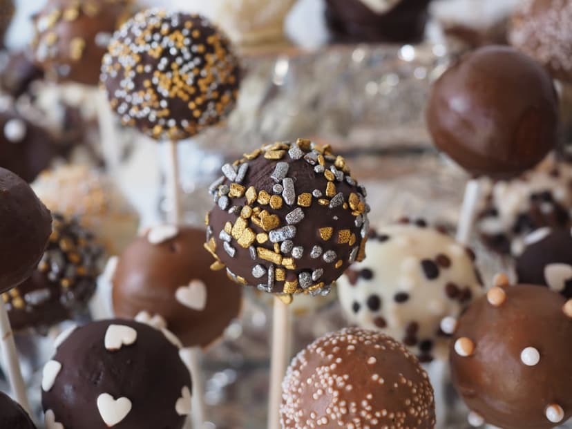 Chocolate cake pops decorated with gold leaf, silver accents, and heart sprinkles arranged on a platter.
