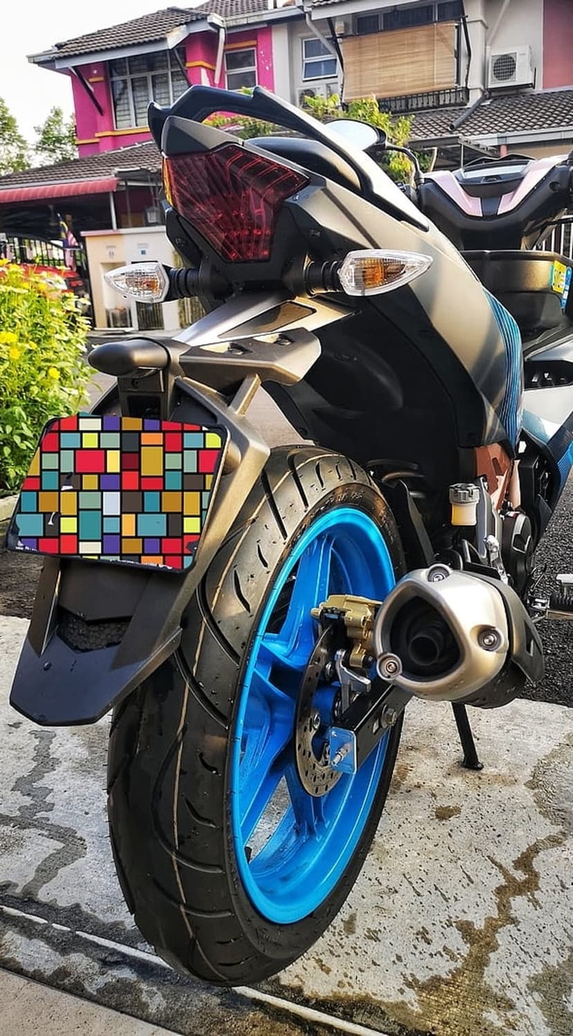 Sport motorcycle tail light and exhaust assembly featuring a vibrant mosaic plate and blue wheel rim detail.