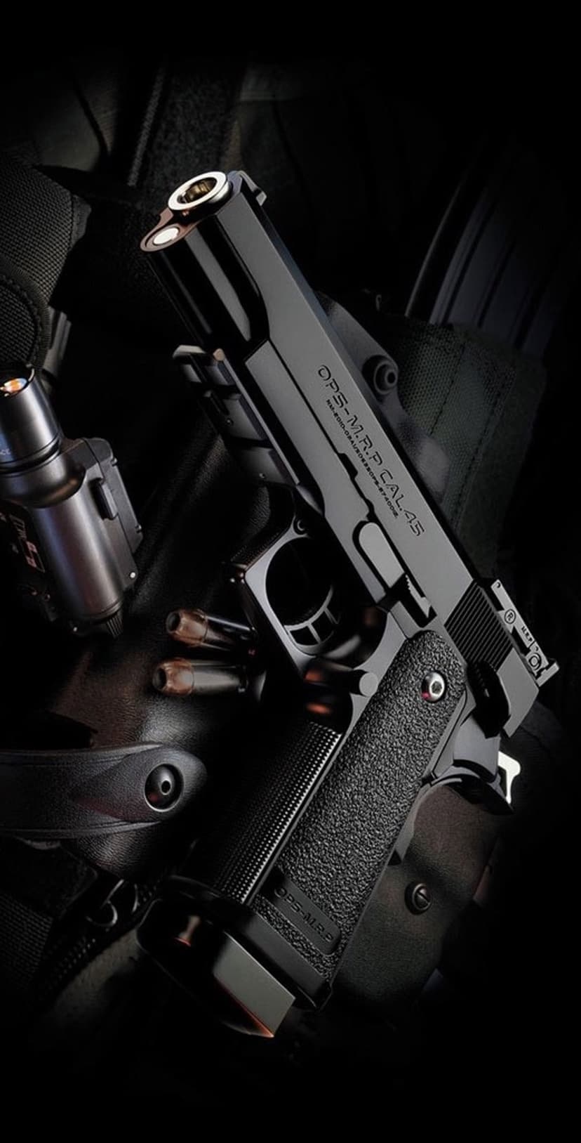 Black tactical handgun with caliber engravings next to three brass bullets and a laser sight on a dark surface.