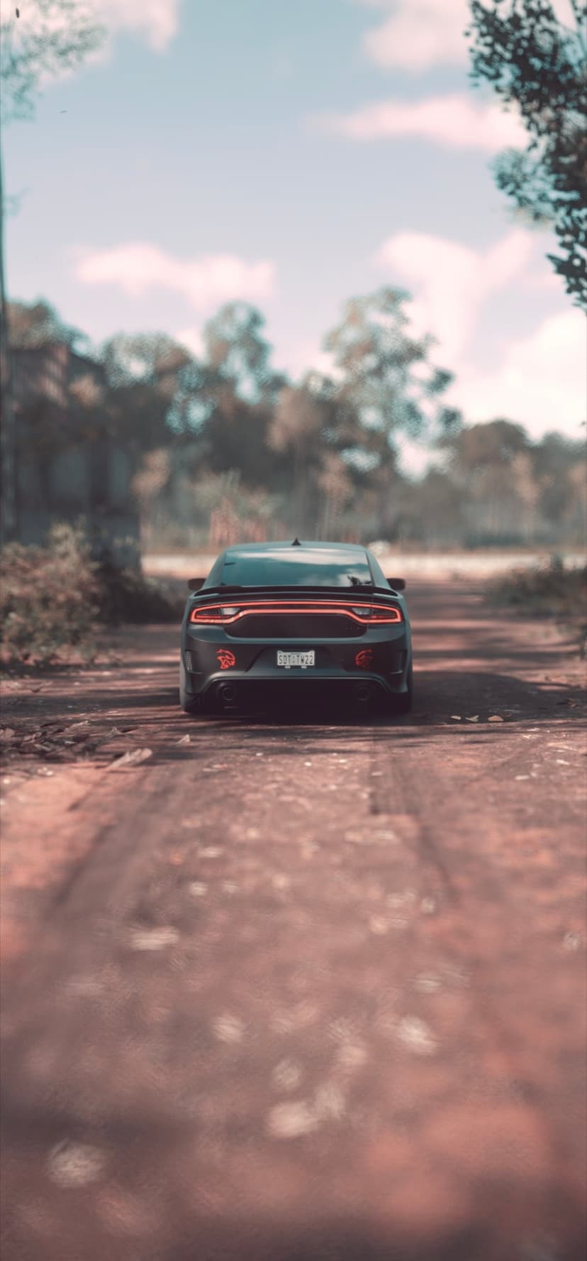 Black Dodge Charger parked on a dirt road at sunset with glowing red taillights surrounded by dark forest trees.