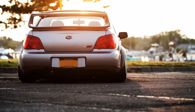 Silver Subaru WRX STI with a widebody kit and rear wing parked at sunset in a scenic landscape orientation.
