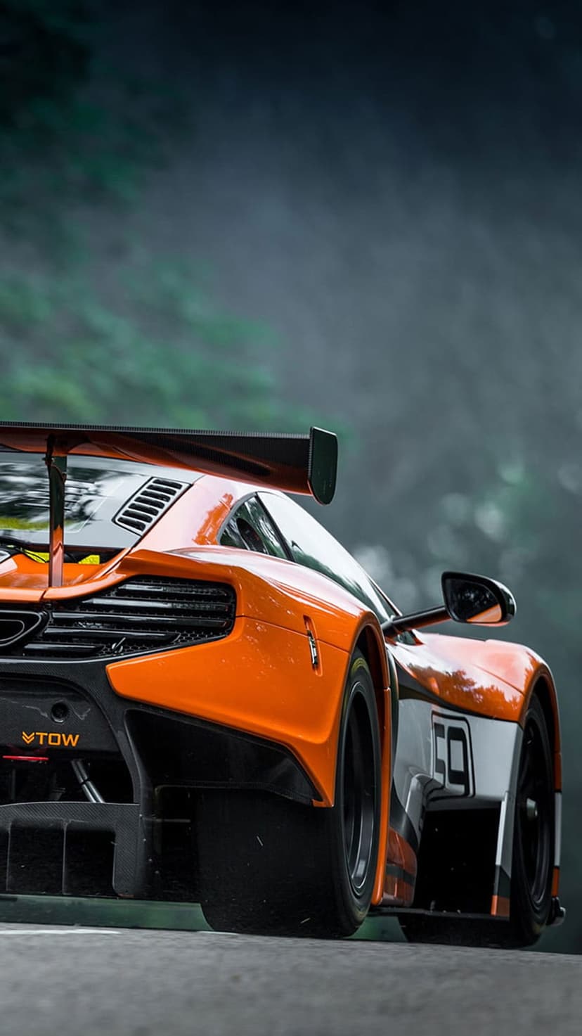 Orange McLaren race car with a large rear wing and number 59 parked on a foggy road with a forest backdrop.