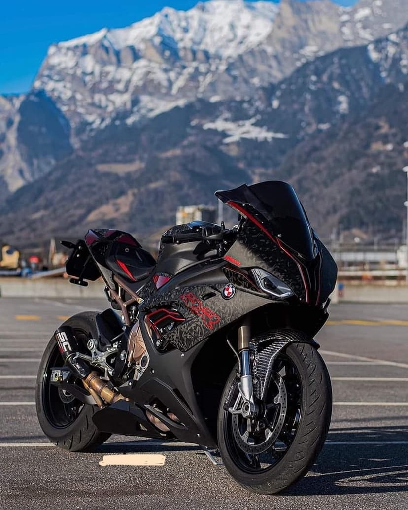 BMW S1000RR motorcycle with carbon fiber parts parked against a backdrop of towering snowy mountain peaks.