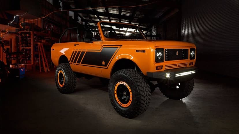 Orange International Scout II off-roader with black stripes and massive tires in a dark garage setting.