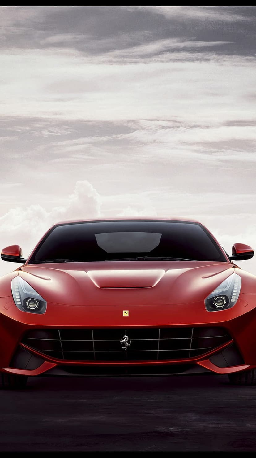 Red Ferrari F12berlinetta with aggressive headlights and front grille parked under a cloudy, overcast sky.