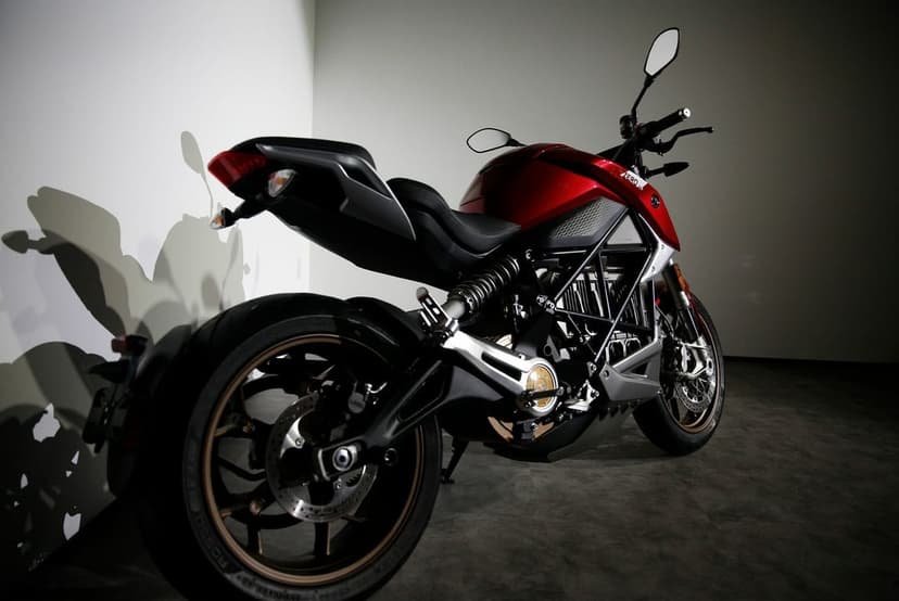 Metallic red electric motorcycle from a low rear angle against a white wall with dramatic shadows in a studio.
