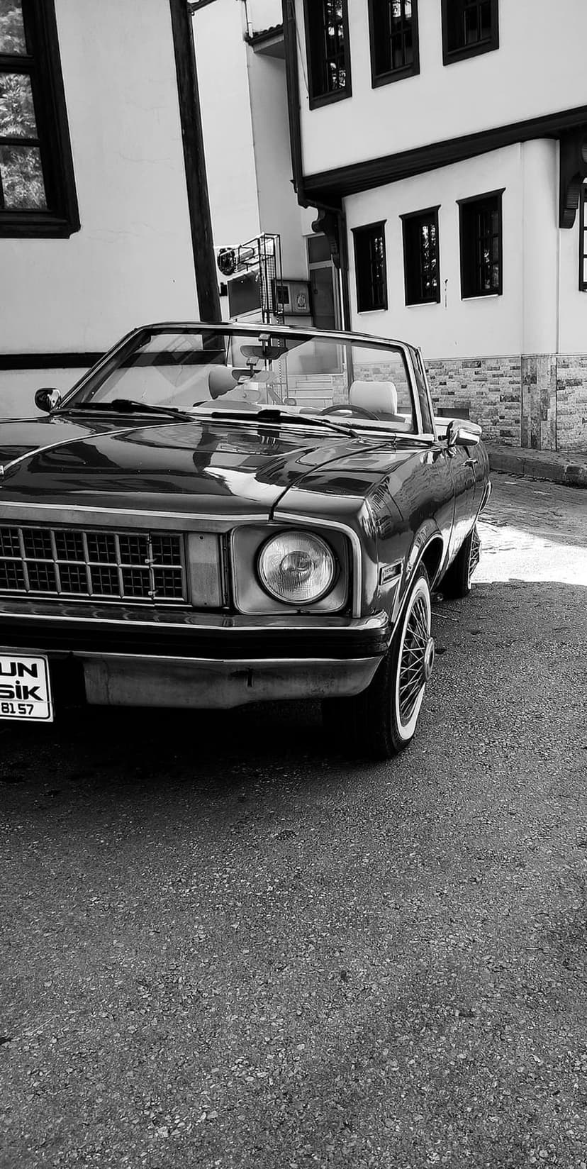Black classic convertible with wire wheels parked on a textured street in front of old European buildings.