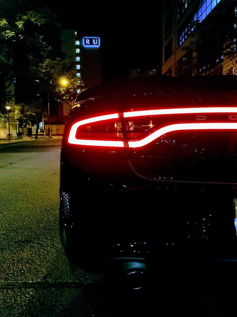 Black sports car rear view with illuminated red LED taillights on a dark urban street at night with city bokeh.