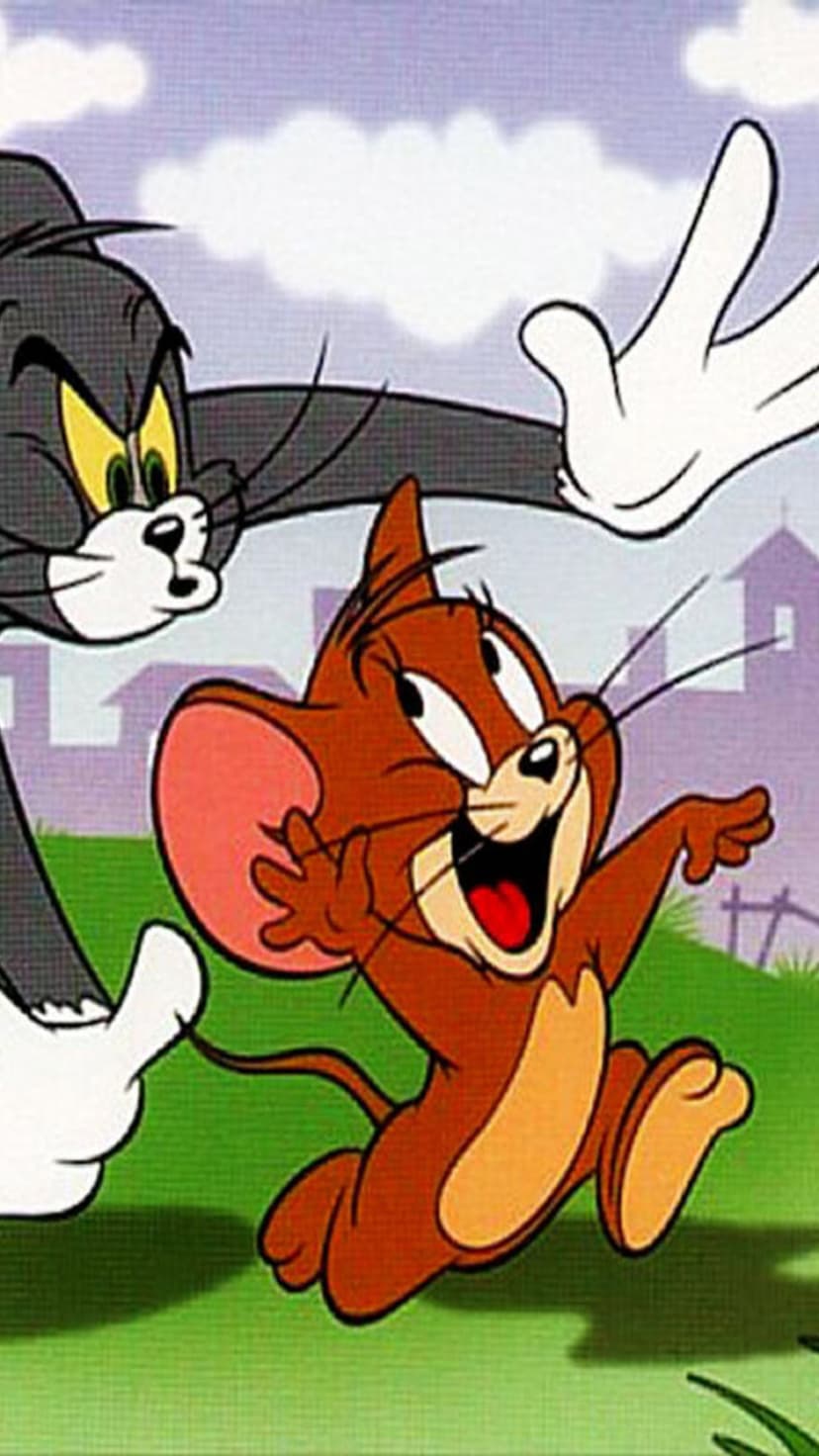 Tom the cat chases Jerry the mouse through a green field with a red barn under a cloudy sky in the background.