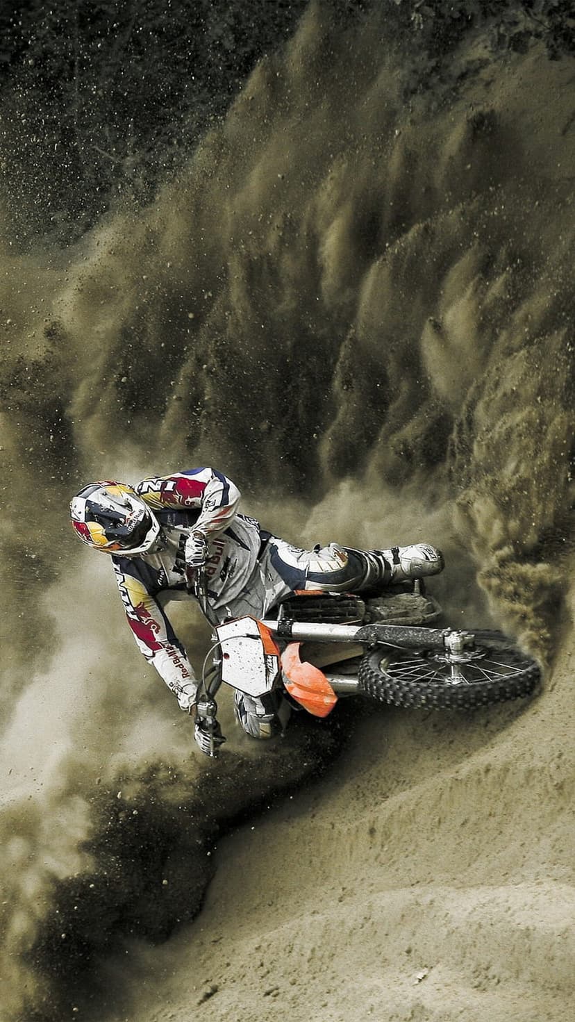 Motocross rider in a racing suit leans through a sharp turn while heavy dust billows from the rear dirt bike tire.