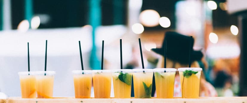 Yellow and orange citrus drinks in clear cups with black straws and mint leaves arranged on a wooden surface.