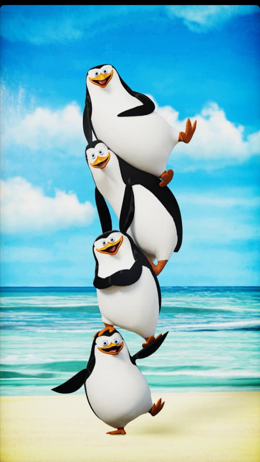 Four penguins stack vertically on a sandy beach under a bright blue sky with fluffy white clouds and ocean waves.