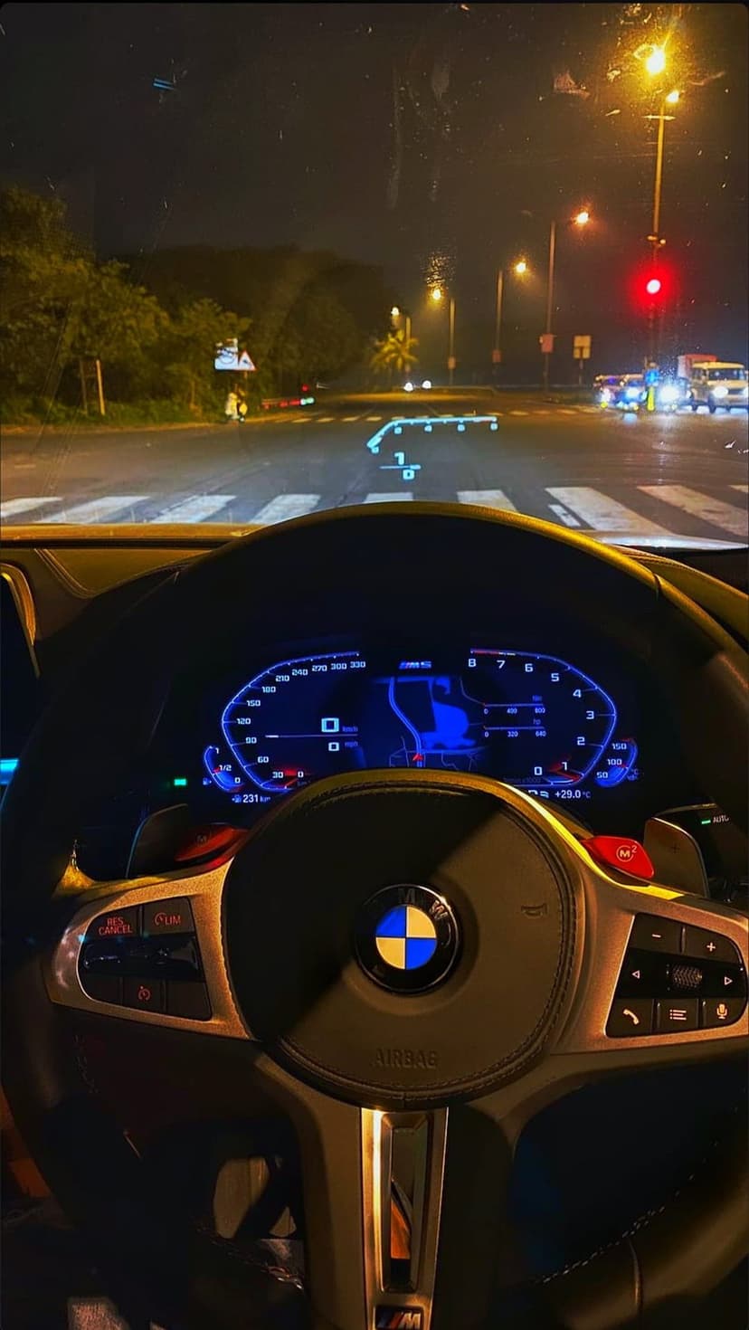 BMW steering wheel and digital dashboard glow in a dark car interior with a head-up display on the glass.