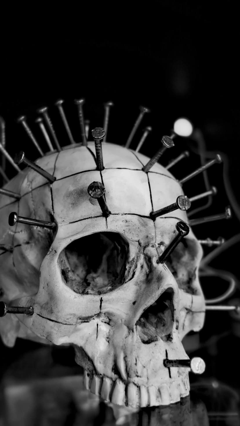 Human skull with metallic nails driven into the bone, featuring high-contrast black and white shadows.