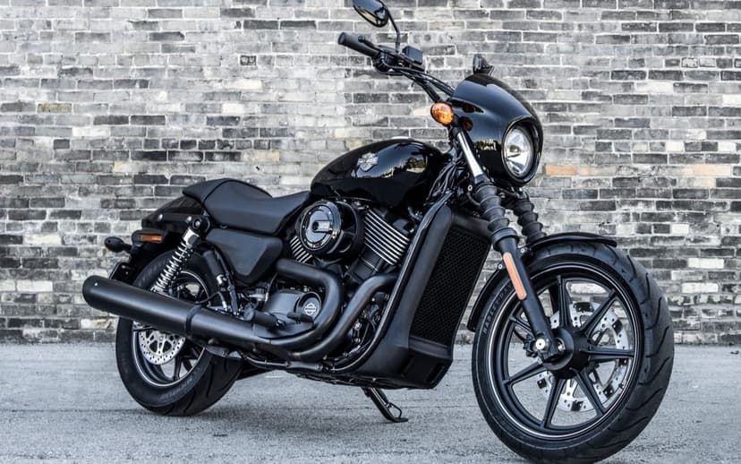 Black Harley-Davidson motorcycle parked on asphalt in front of a weathered grey brick wall in daylight.
