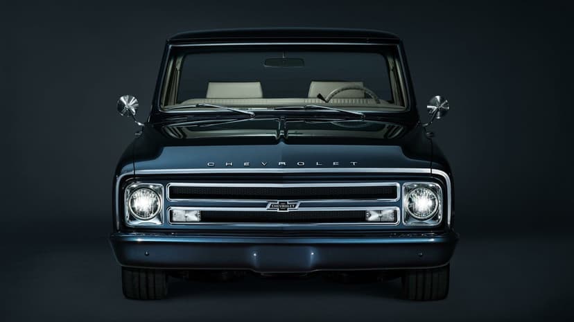 Front view of a dark blue vintage Chevrolet truck with chrome grille and glowing headlights in a dark studio.