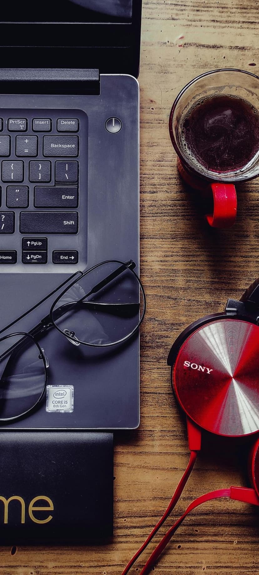 Red headphones, a coffee glass, and a laptop rest on a rustic wooden table in a flat lay vertical composition.