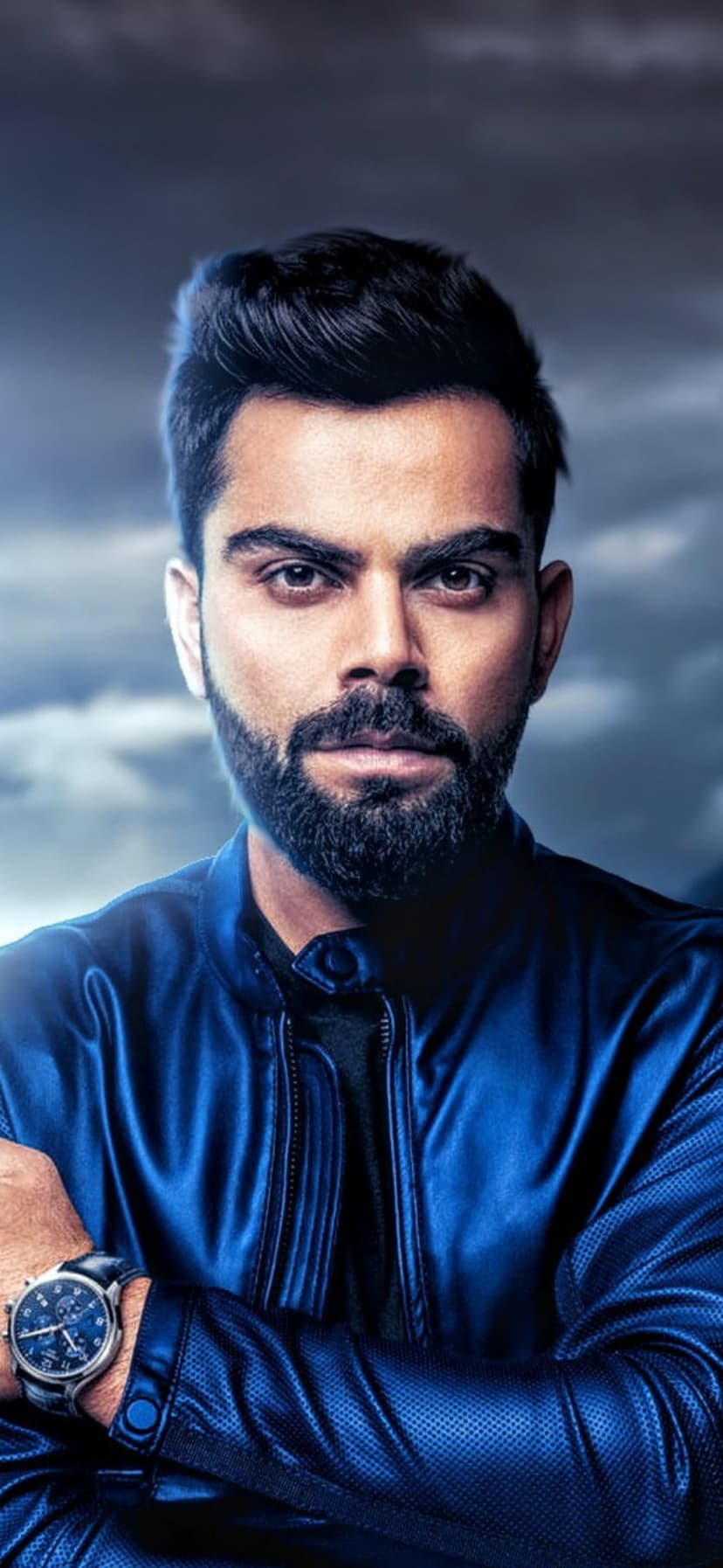 Virat Kohli wearing a blue jacket with crossed arms against a dramatic cloudy sky in a vertical portrait.