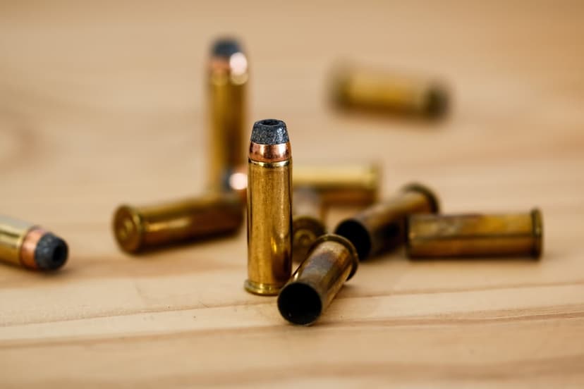 Brass bullets with metallic primers rest on a light wood grain surface with a soft-focus background.