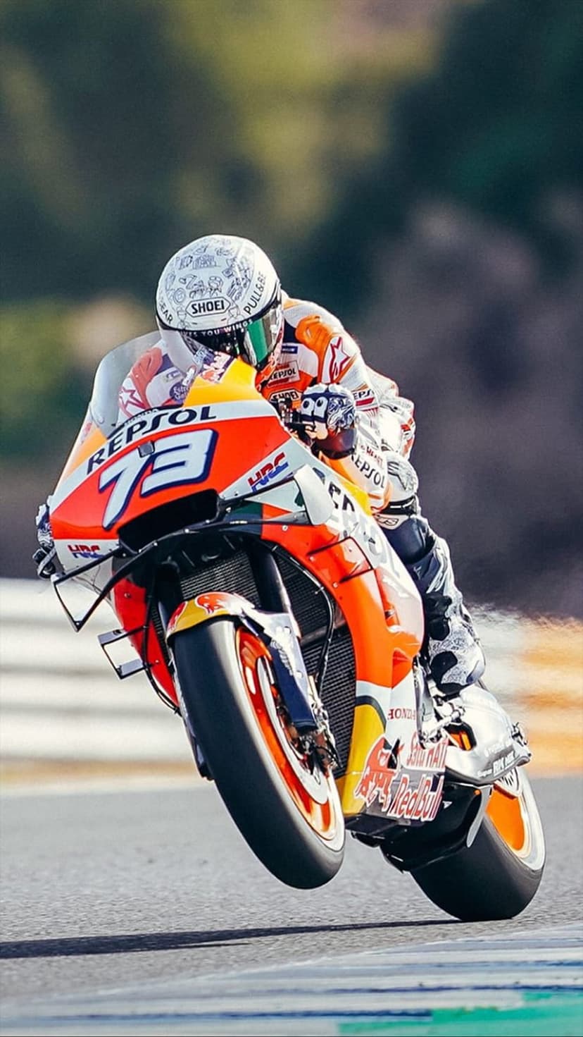 Motorcycle racer in an orange Repsol Honda suit leans low into a track turn with a white helmet and racing bike.