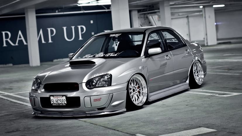 Silver modified Subaru WRX STI with deep-dish chrome wheels parked in a concrete underground garage.