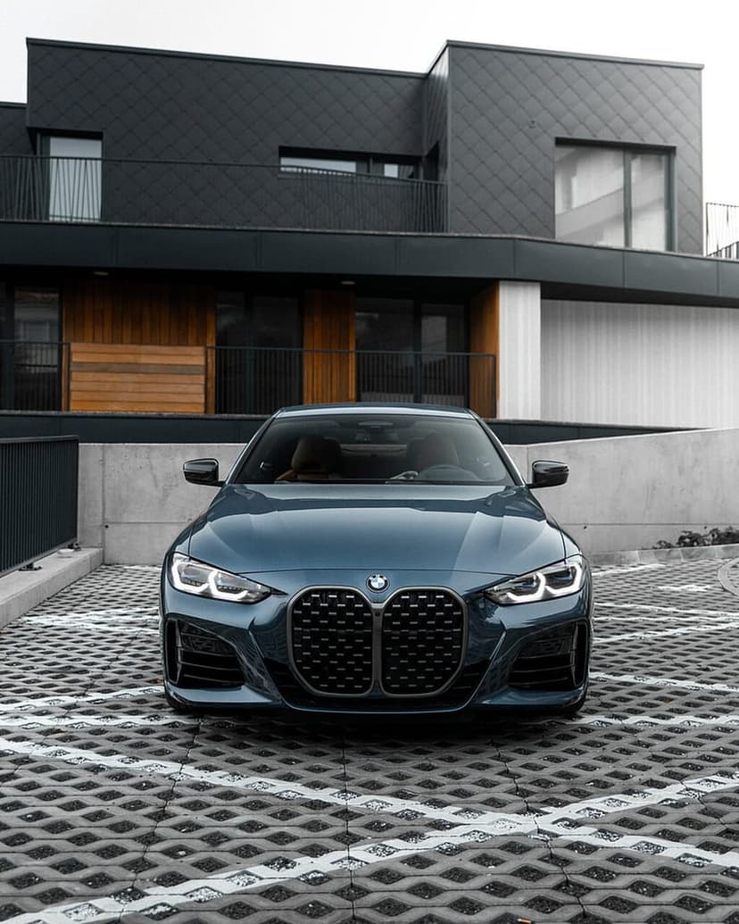 Blue BMW sedan parked on geometric stone pavers in front of a modern house with wood and glass accents.