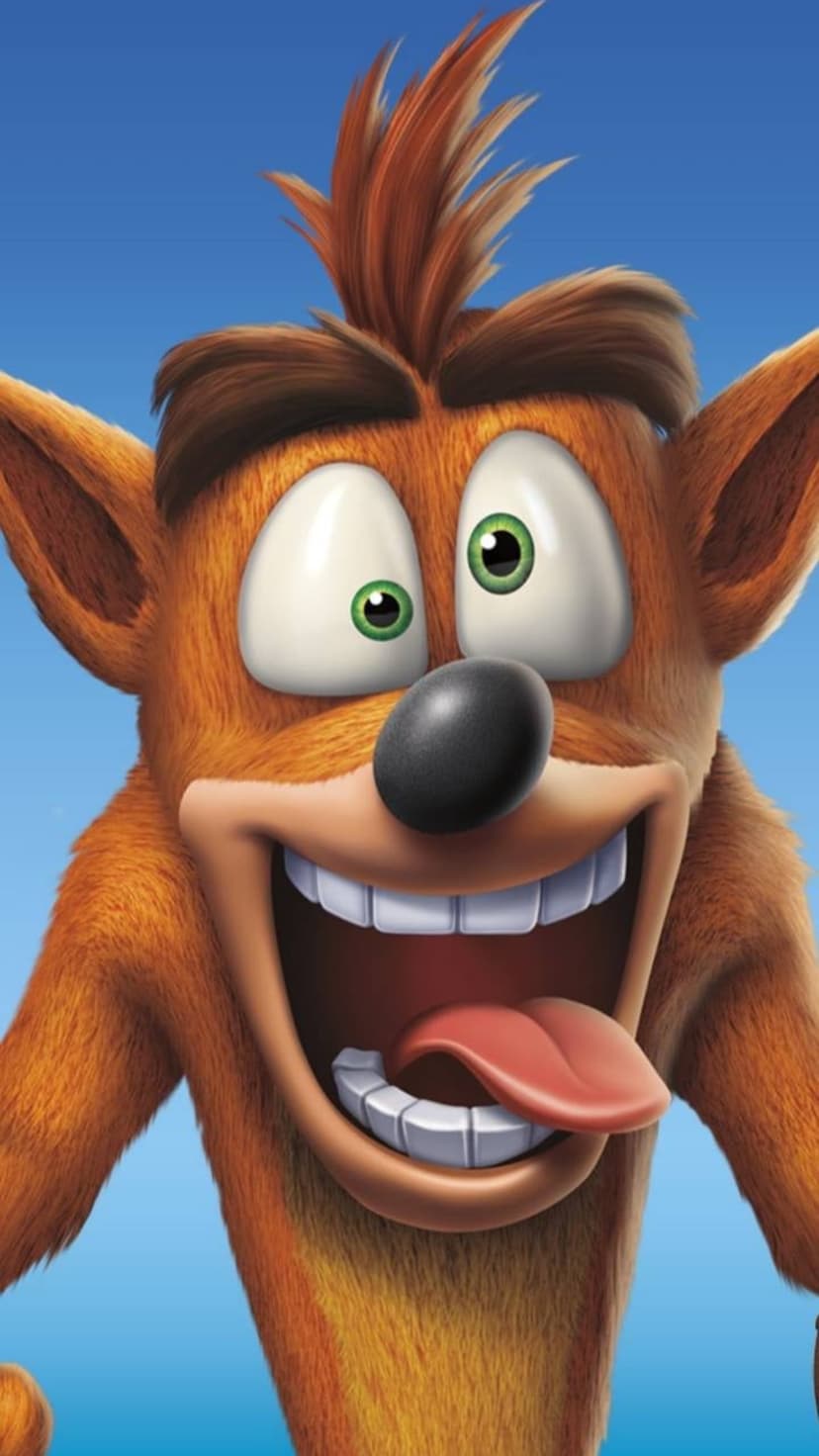 Crash Bandicoot grinning with his tongue out against a blue sky, featuring his orange fur and expressive eyes.