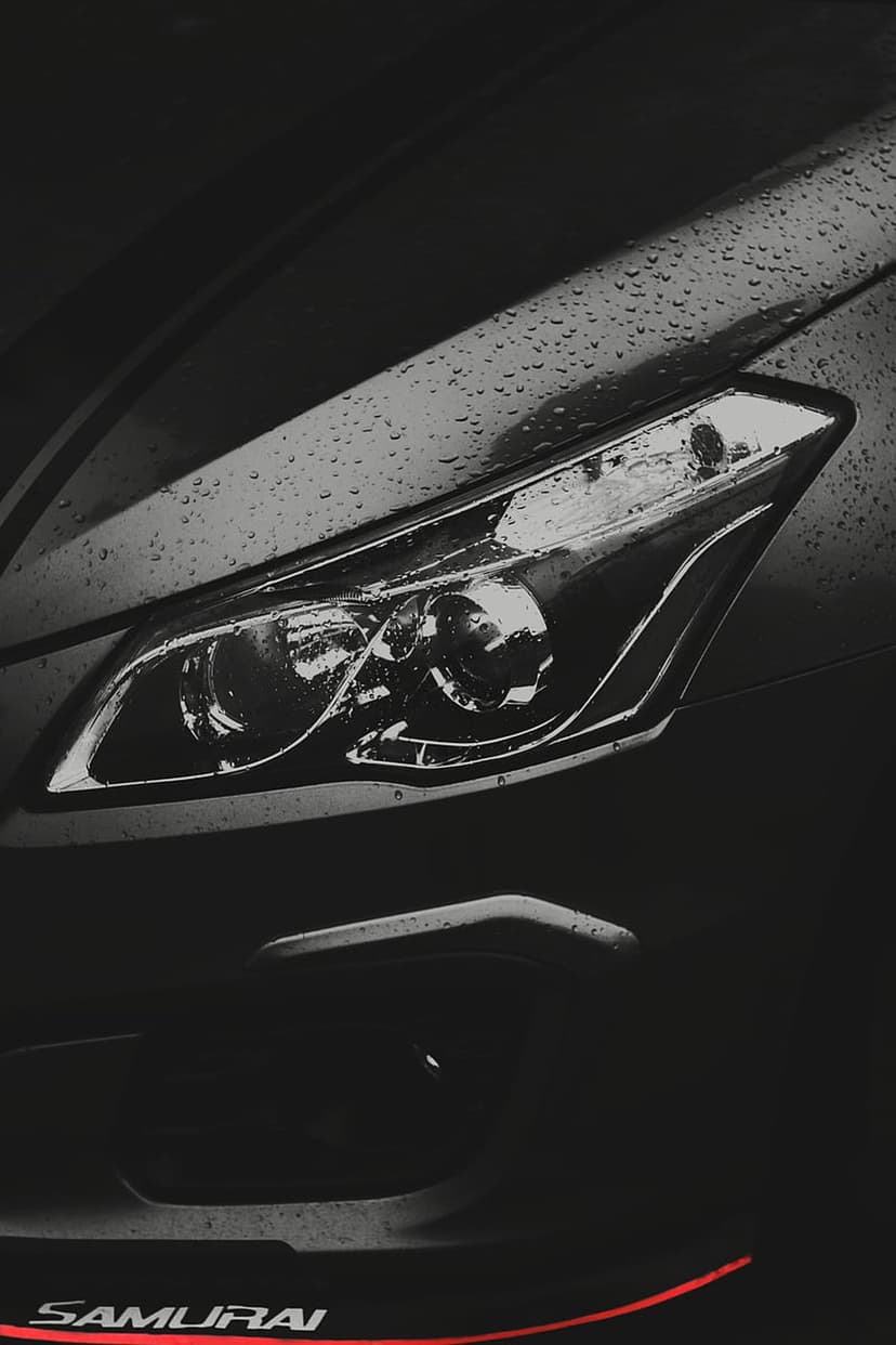 Black car headlight covered in rain droplets with a red stripe and white Samurai text on the lower bumper.