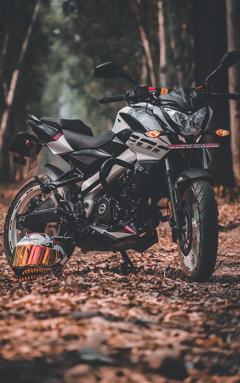 White sportbike and reflective helmet rest on a rustic woodland path covered in vibrant orange autumn leaves.