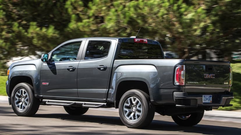 Dark gray GMC Canyon pickup truck driving on a road with motion-blurred green trees in the background.