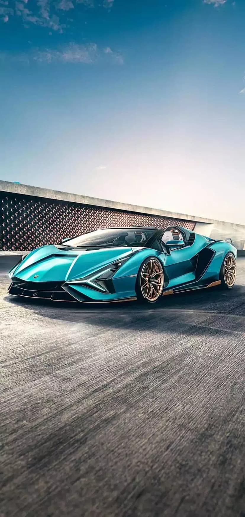 Teal Lamborghini Sian Roadster with gold wheels parked on a track against a modern building and blue sky.