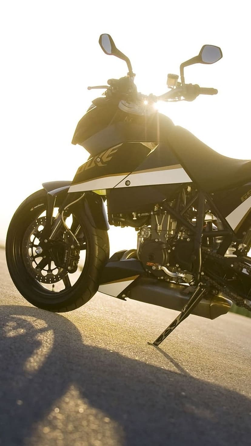 Black and white KTM motorcycle parked on a sunlit asphalt road with a bright lens flare during golden hour.