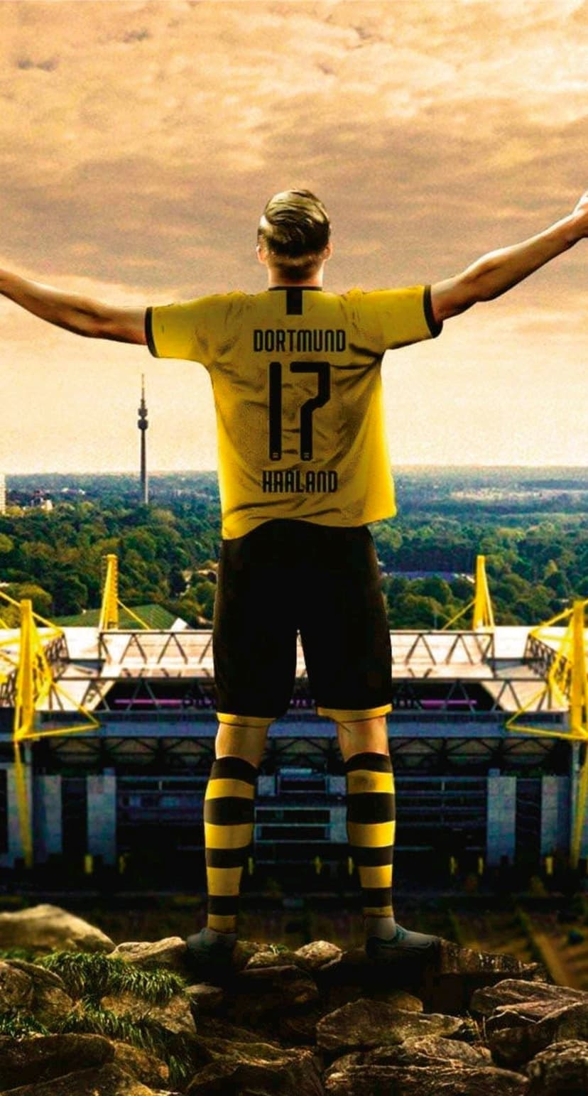 Erling Haaland stands with arms outstretched in a yellow BVB kit before Signal Iduna Park and a sunset sky.