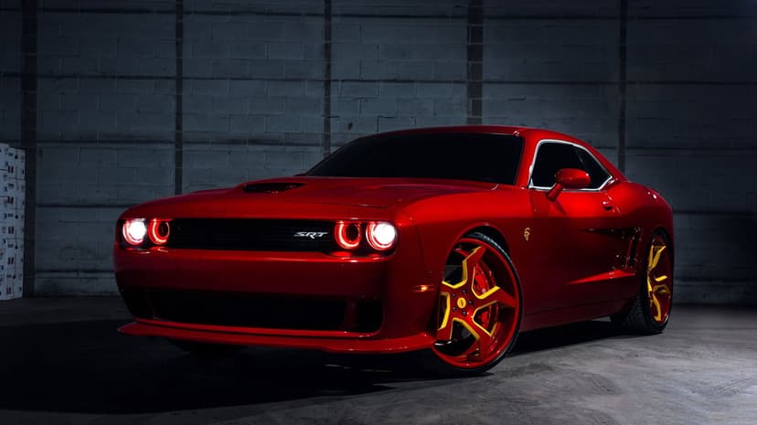 Red Dodge Challenger SRT with yellow-accented wheels and red halo headlights against a dark grey brick wall.