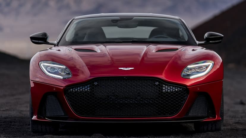Front view of a metallic red sports car with illuminated LED headlights parked on dark rocky terrain.