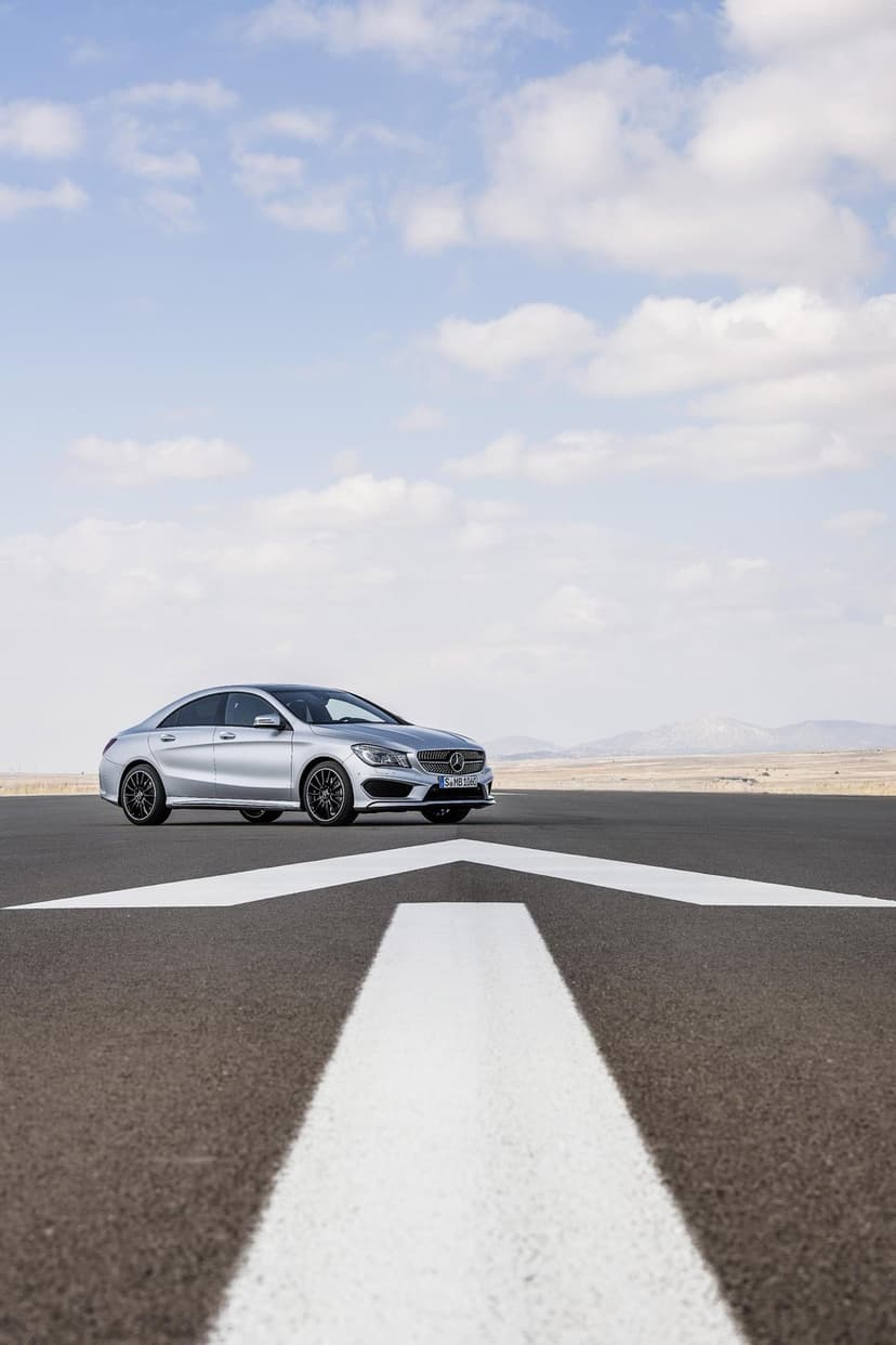 Silver Mercedes-Benz sedan on an asphalt runway with a large white arrow under a bright cloudy blue sky.