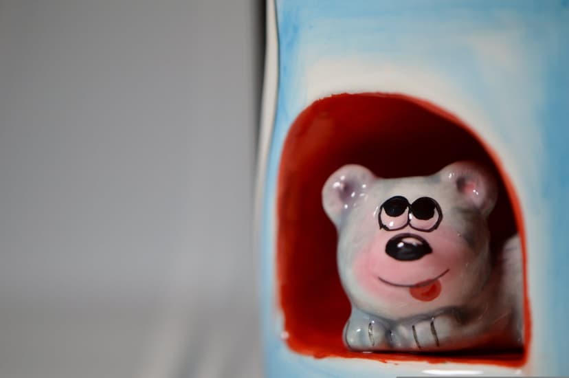 Ceramic bear with a pink tongue peeks from a red cave opening against a soft blue background in a macro shot.