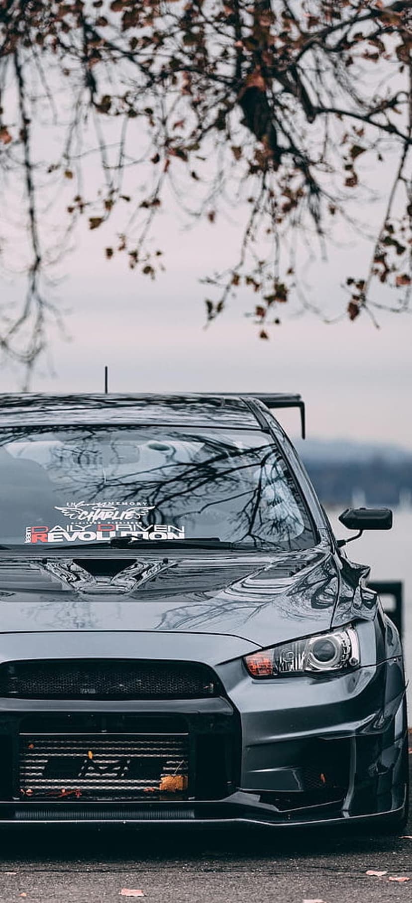 Mitsubishi Lancer Evolution X front bumper and intercooler parked on a leaf-strewn road under overcast skies.