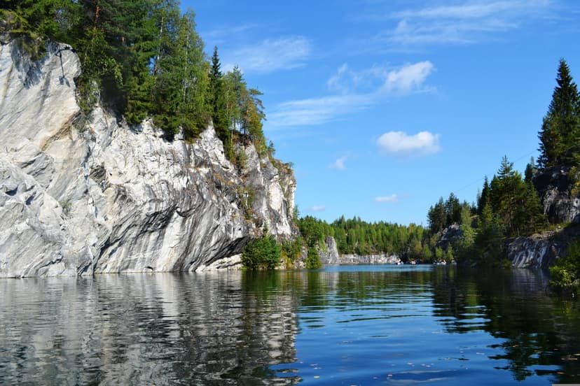 Towering marble cliffs and green pines reflect in a tranquil lake under a blue sky for a vertical mobile view.