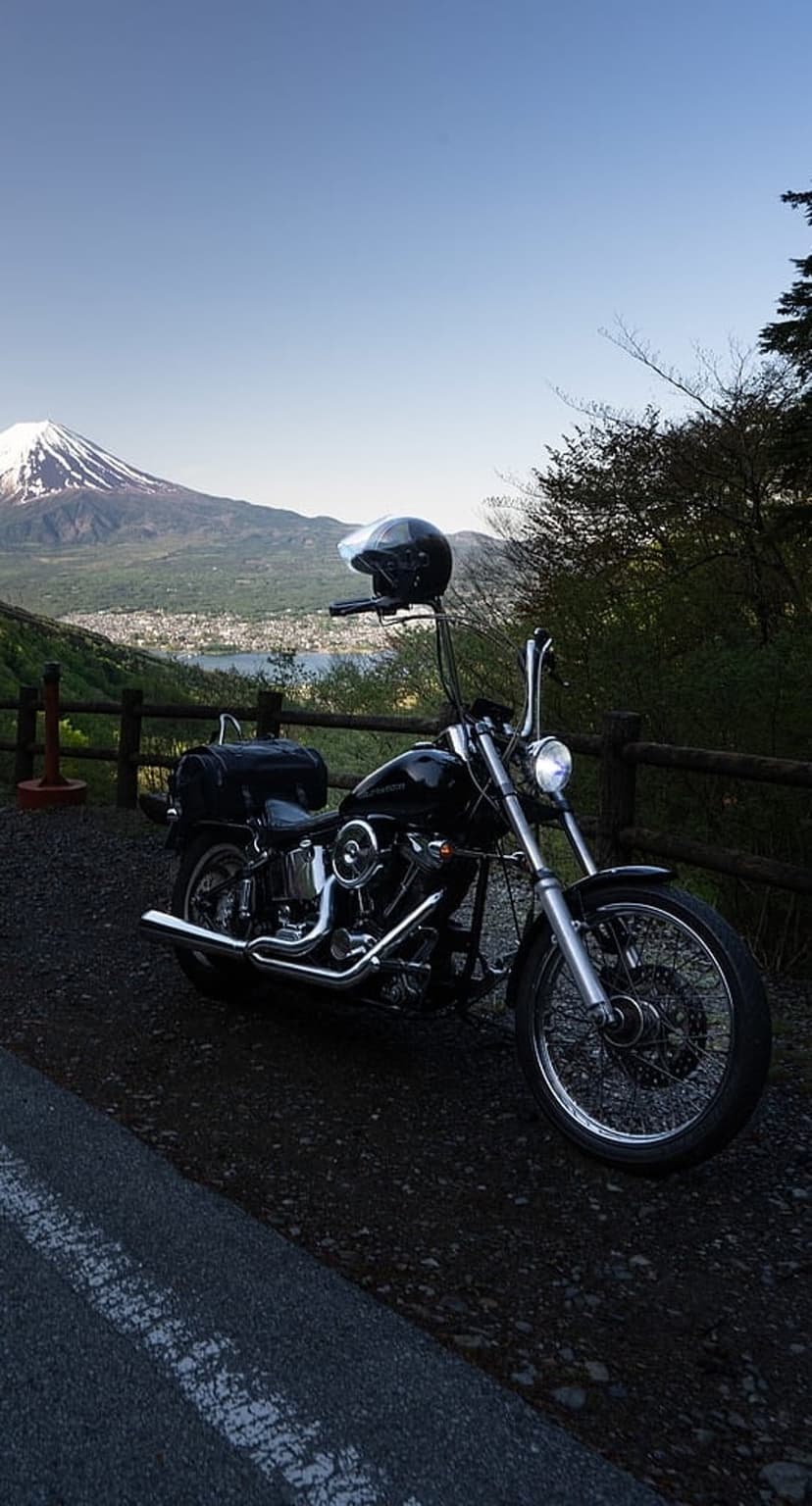 Black Harley-Davidson motorcycle parked on a gravel path facing Mount Fuji across a calm lake in Japan.