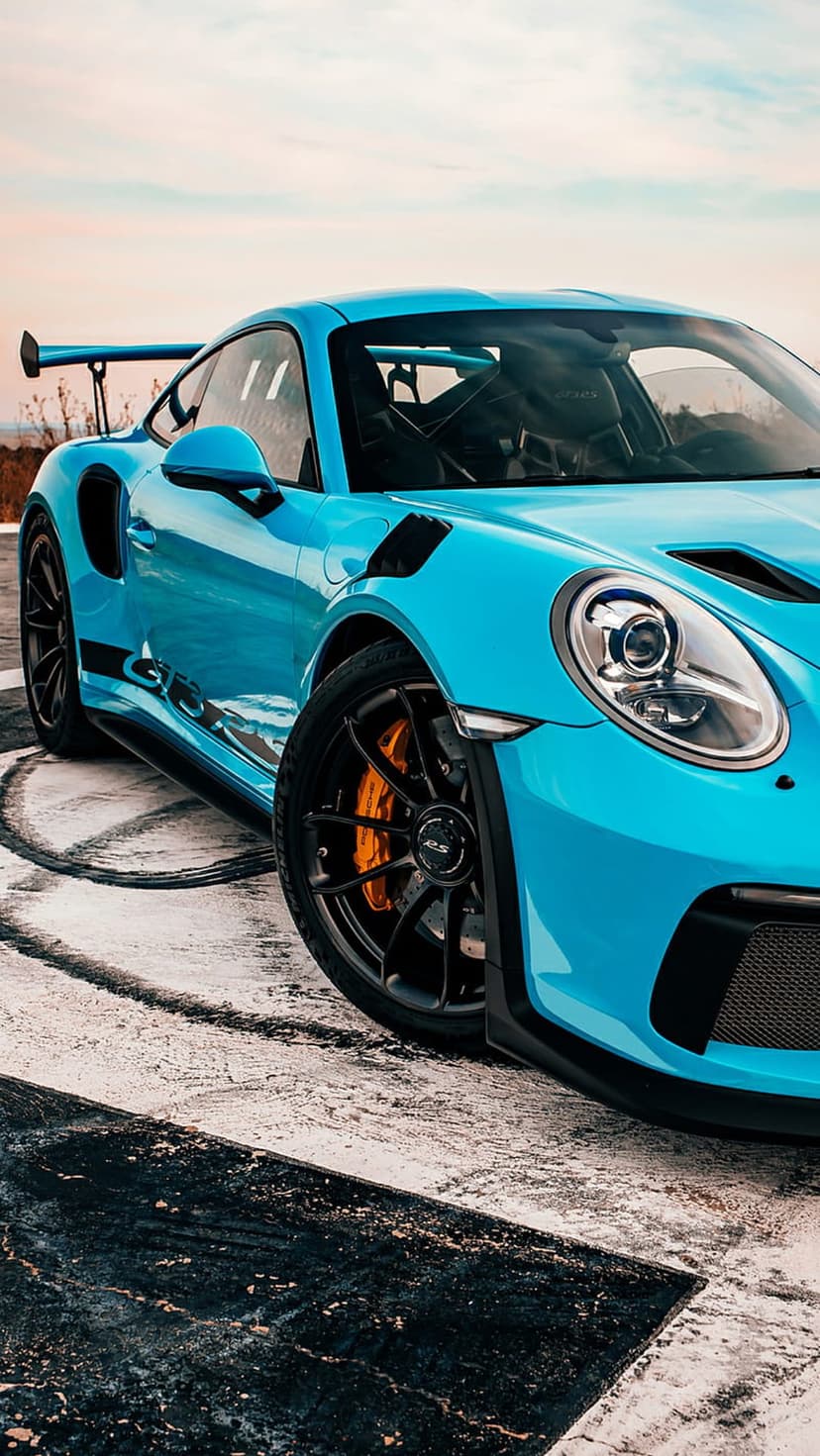 Blue Porsche 911 GT3 RS side profile on an asphalt track featuring a large rear wing and aerodynamic vents.