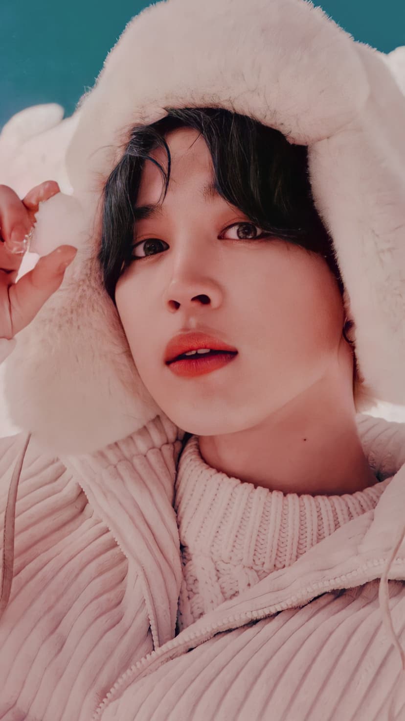 Jimin from BTS wears a fuzzy white winter hat and cream sweater while holding a snowball against a blue background.