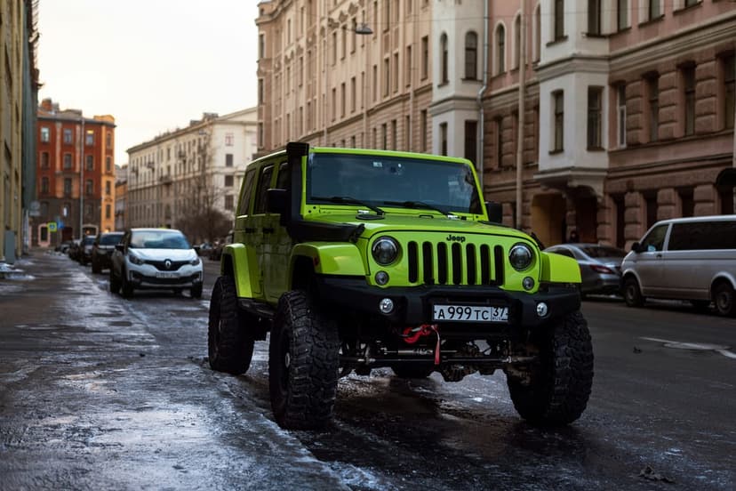 Lime green Jeep Wrangler with off-road tires parked on a wet street near European buildings under a cloudy sky.