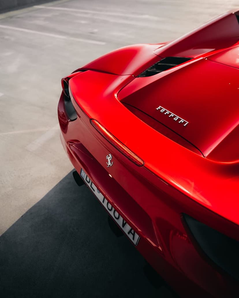 Red Ferrari rear deck features a chrome emblem and glowing taillights set against polished crimson bodywork.
