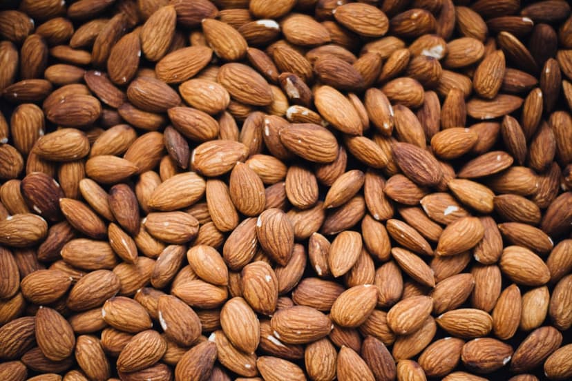 Raw almonds with brown skins are piled together in a macro overhead view showing varied oval shapes and textures.