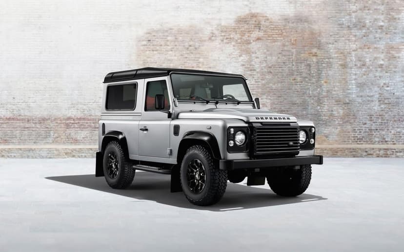 Silver Land Rover Defender 90 with black roof parked against a rustic brick wall in an industrial studio.