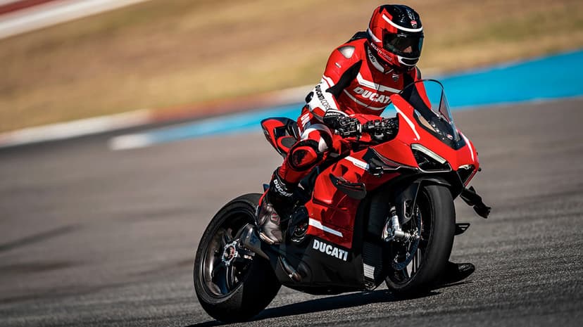 Red Ducati sportbike leaning into a corner on a racetrack with a rider in red and white leathers.
