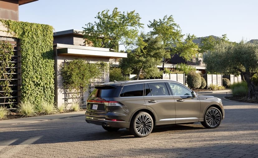 Bronze Lincoln Aviator SUV parked on a paved driveway in front of a modern home with green ivy walls.