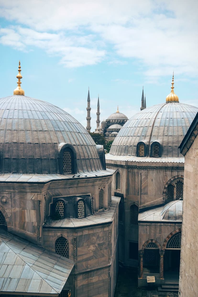 Blue Mosque domes and slender minarets stand under a cloudy blue sky in a vertical Istanbul city view.