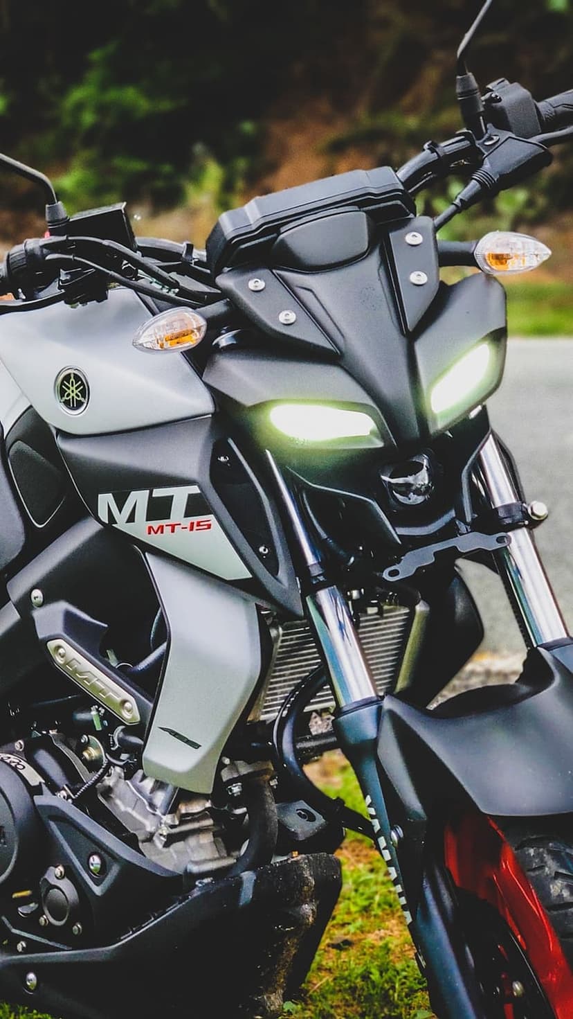 Yamaha MT-15 motorcycle front view featuring glowing LED headlights, matte black fairing, and metallic engine parts.